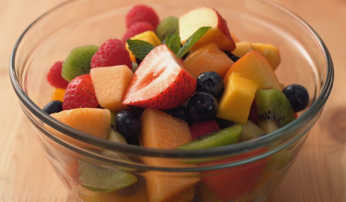 Staklena činija sa mešanim svežim voćem.